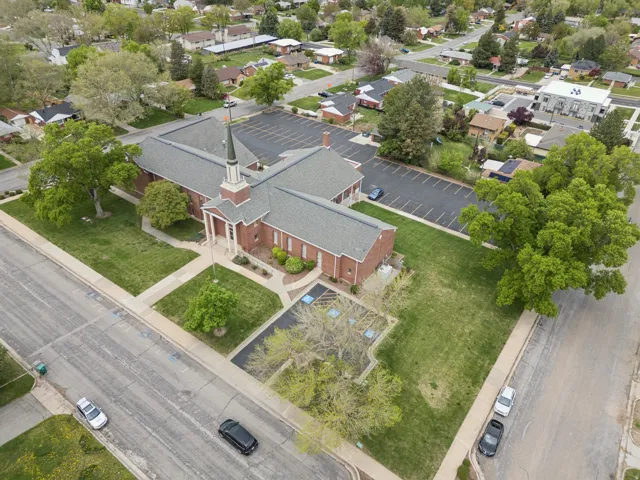 Brick building featuring a prominent steeple, multiple entrances, and a large paved parking lot.