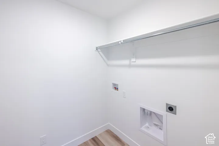 Utility space featuring wood-finish flooring, white walls, built-in overhead shelving with a clothing rod, and dedicated washer and dryer hookups