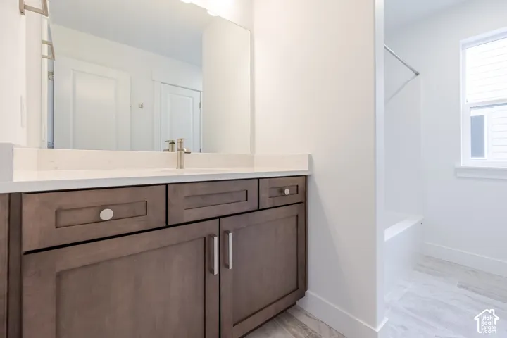 Bathroom featuring a vanity with dark-finish cabinetry, light stone-surface countertop, integrated rectangular sink, brushed-metal faucet, and a large wall-mounted mirror