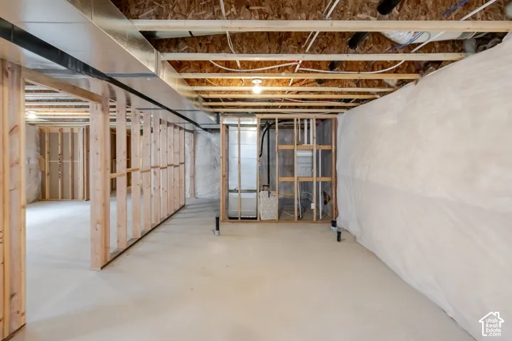 Unfinished area featuring exposed wooden framing, concrete flooring, exposed ceiling joists, white vapor barrier wall covering, and a metal HVAC unit