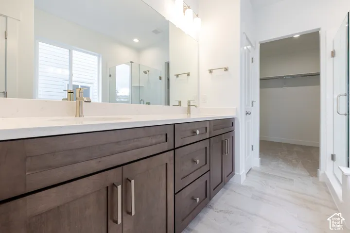 Dual-sink vanity with light-toned solid surface countertop and metallic fixtures, complemented by a large wall-mounted mirror, three-light vanity fixture, dark wood-finish cabinetry, and tiled flooring