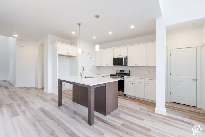 Kitchen featuring white cabinetry, wood-finish flooring, a central island with a stone-top surface, stainless steel appliances, and recessed lighting