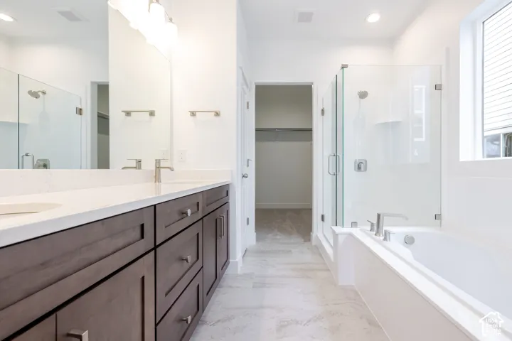 Bathroom featuring a dual-sink vanity with stone countertops, a glass-enclosed shower, a separate soaking tub, and tile flooring