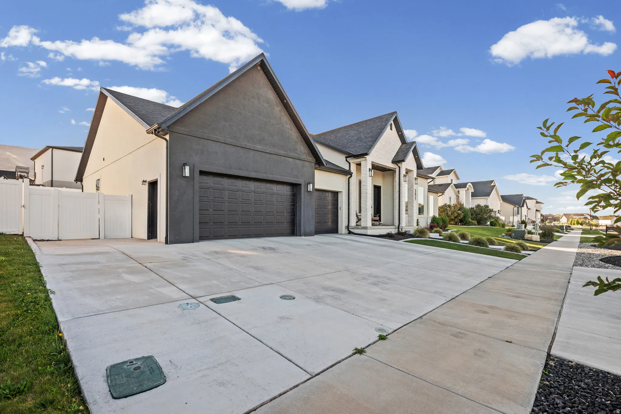 Contemporary exterior with a prominent two-car garage, an additional single-car garage, a wide concrete driveway, white vinyl fencing, and a manicured front lawn with landscaping