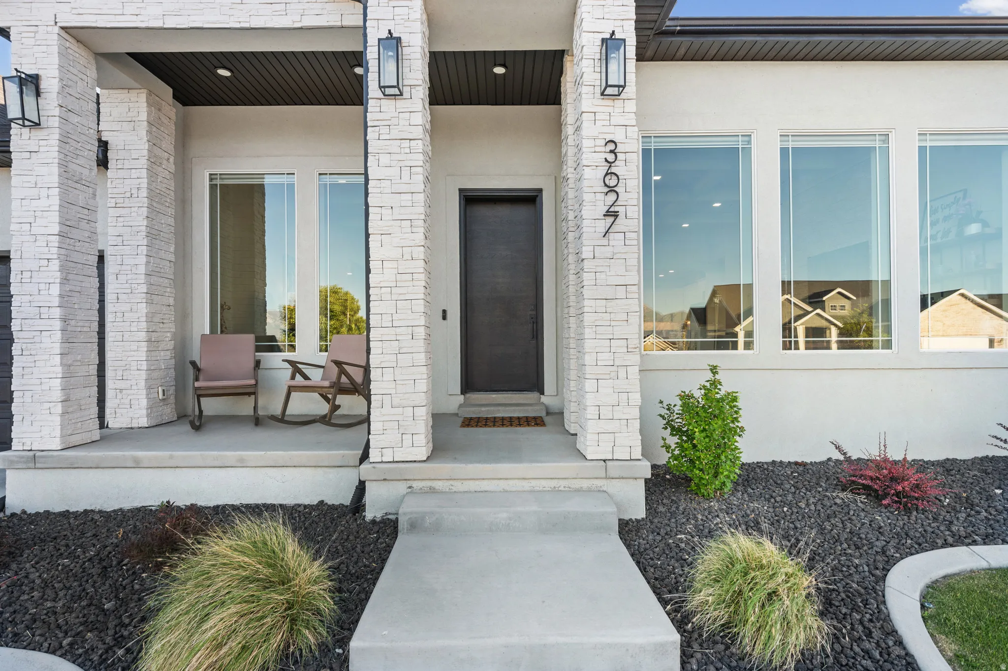 Modern facade featuring stacked stone columns, a dark wood-finish entry door, and large picture windows