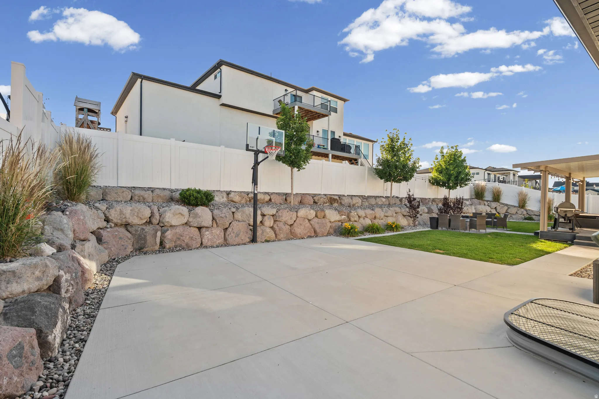 Expansive concrete patio with integrated green space, bordered by a stone retaining wall
