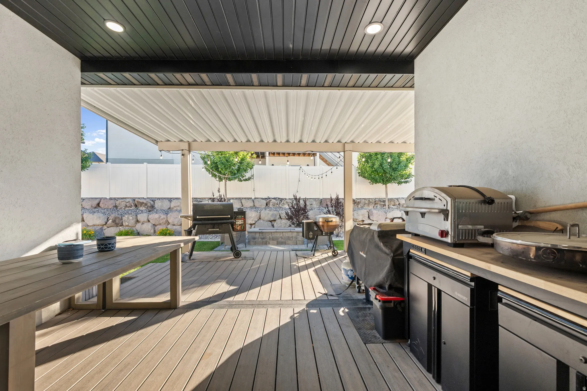 Covered outdoor patio featuring wood-finish decking, a built-in outdoor kitchen with black cabinetry and light wood-finish countertops, a corrugated metal patio cover, and recessed lighting