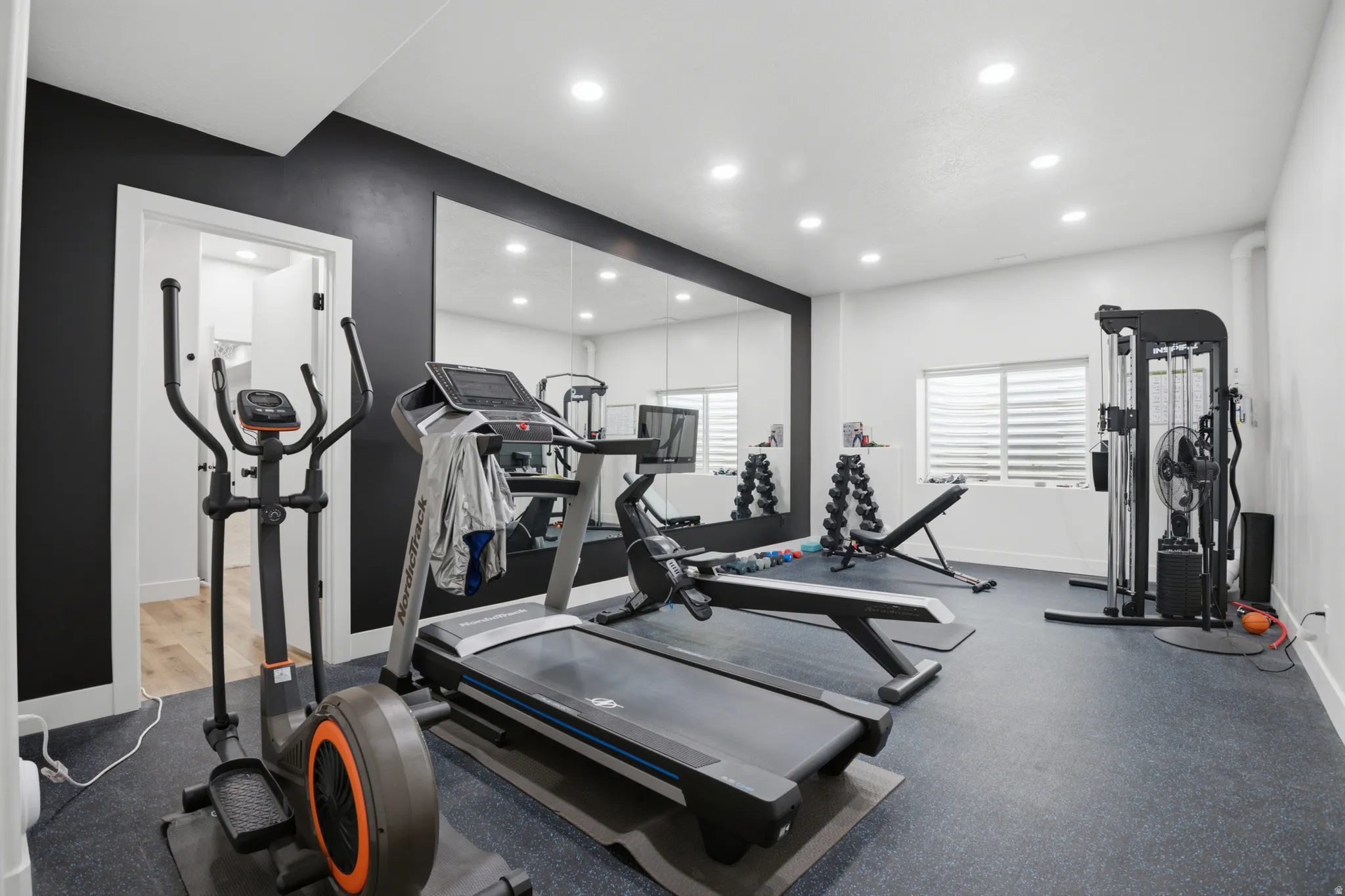 Dedicated fitness space featuring resilient flooring, recessed ceiling lighting, a large wall-mounted mirror, and a window with horizontal blinds