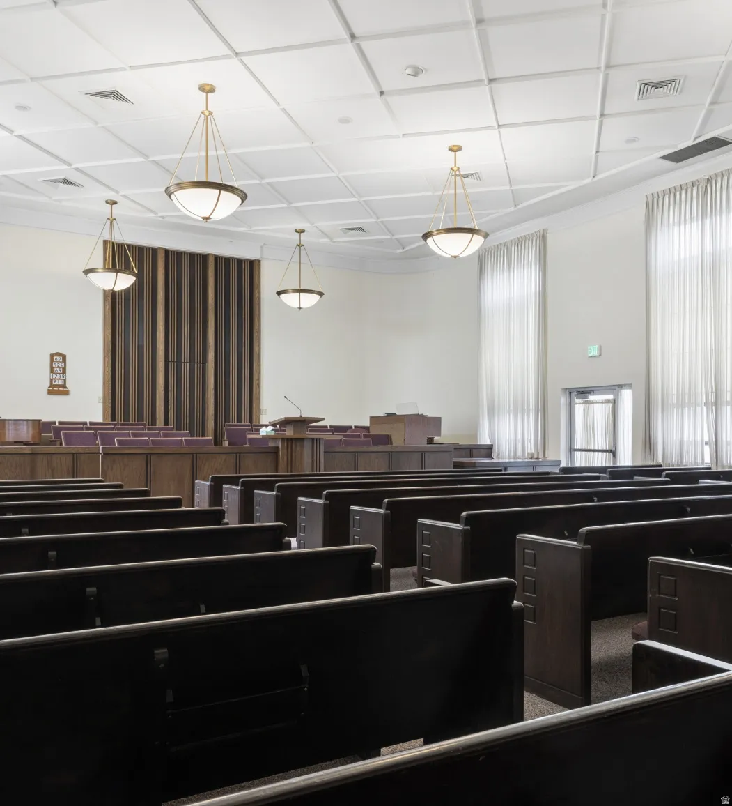 Spacious hall featuring dark wood-finish pews and a patterned drop ceiling with recessed lighting.