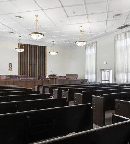 Spacious hall featuring dark wood-finish pews and a patterned drop ceiling with recessed lighting.