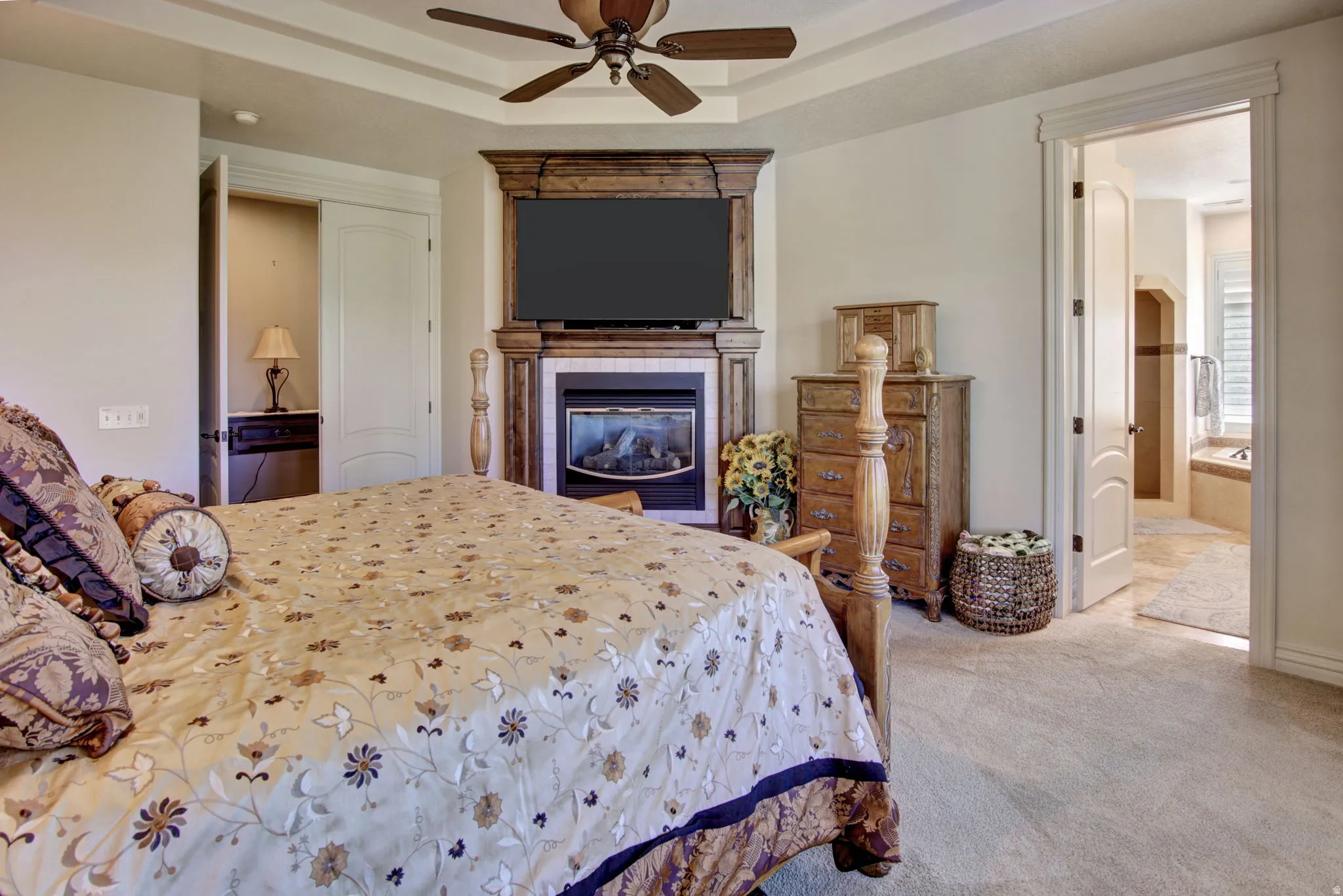 Tray ceiling bedroom featuring a fireplace with a wood-finish mantel and a ceiling fan