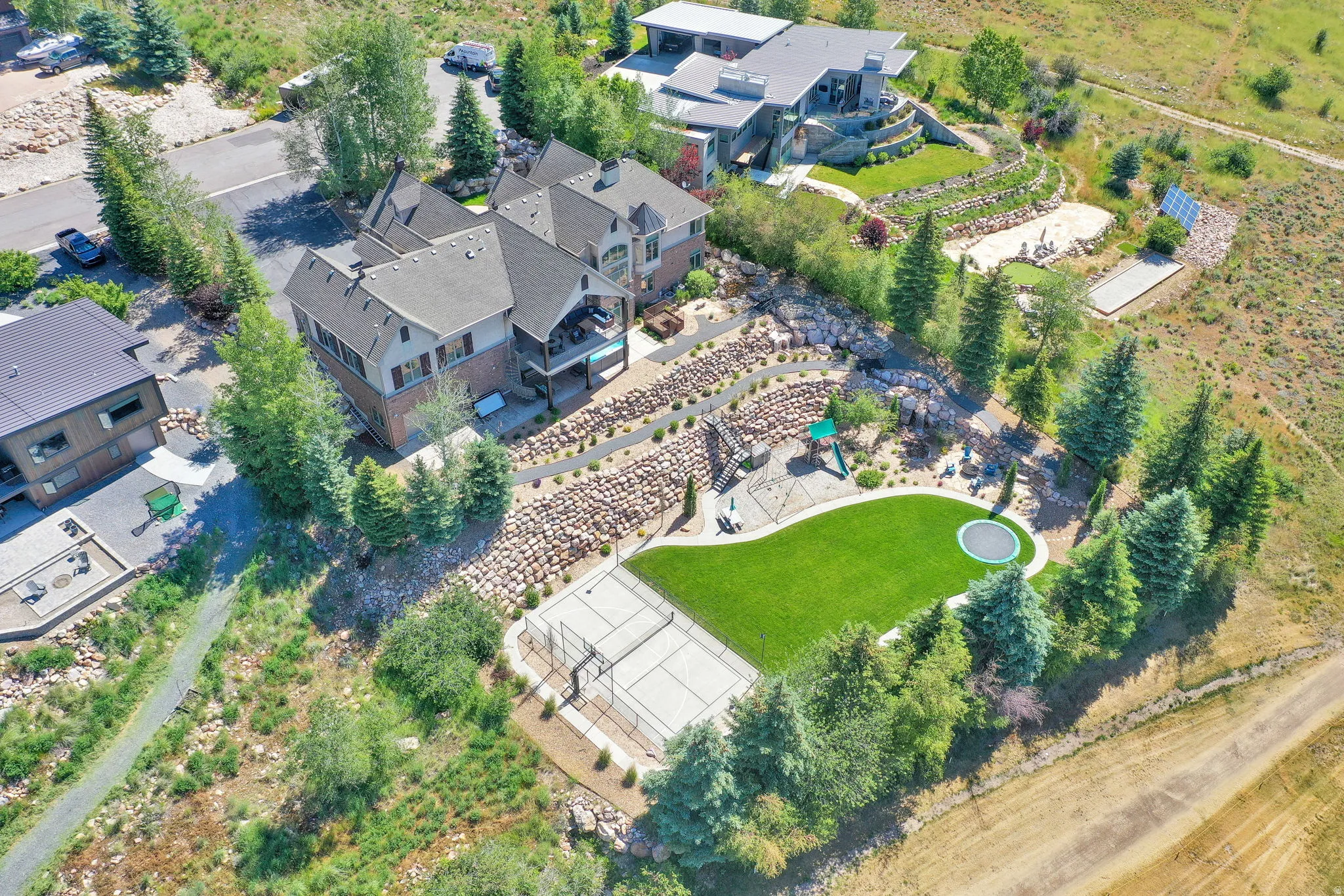 Expansive terraced yard featuring a pickleball court, artificial turf lawn with in-ground trampoline, and a playground structure