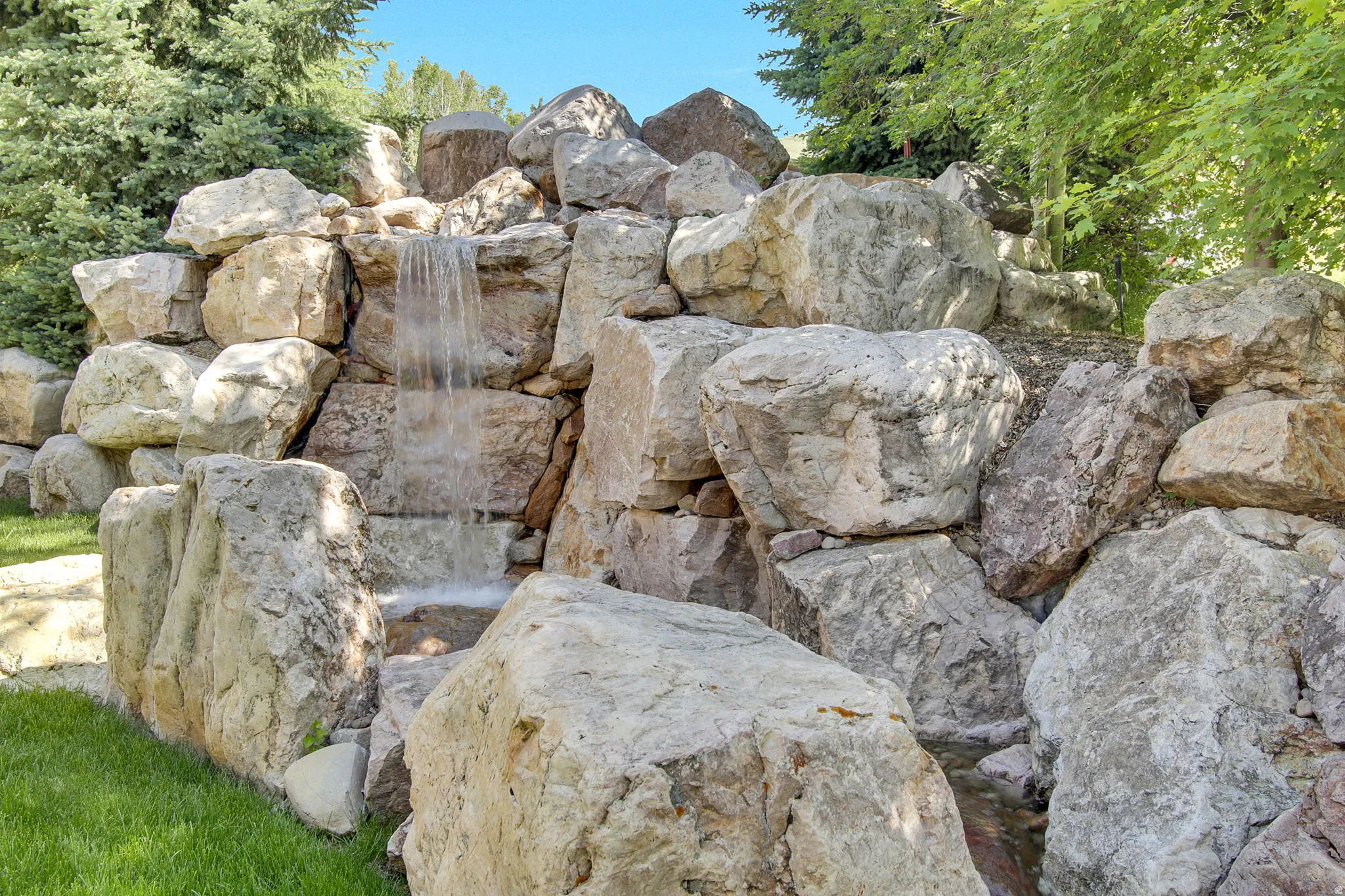 Custom rock waterfall feature with multi-tiered cascades, surrounded by natural boulders and verdant landscaping