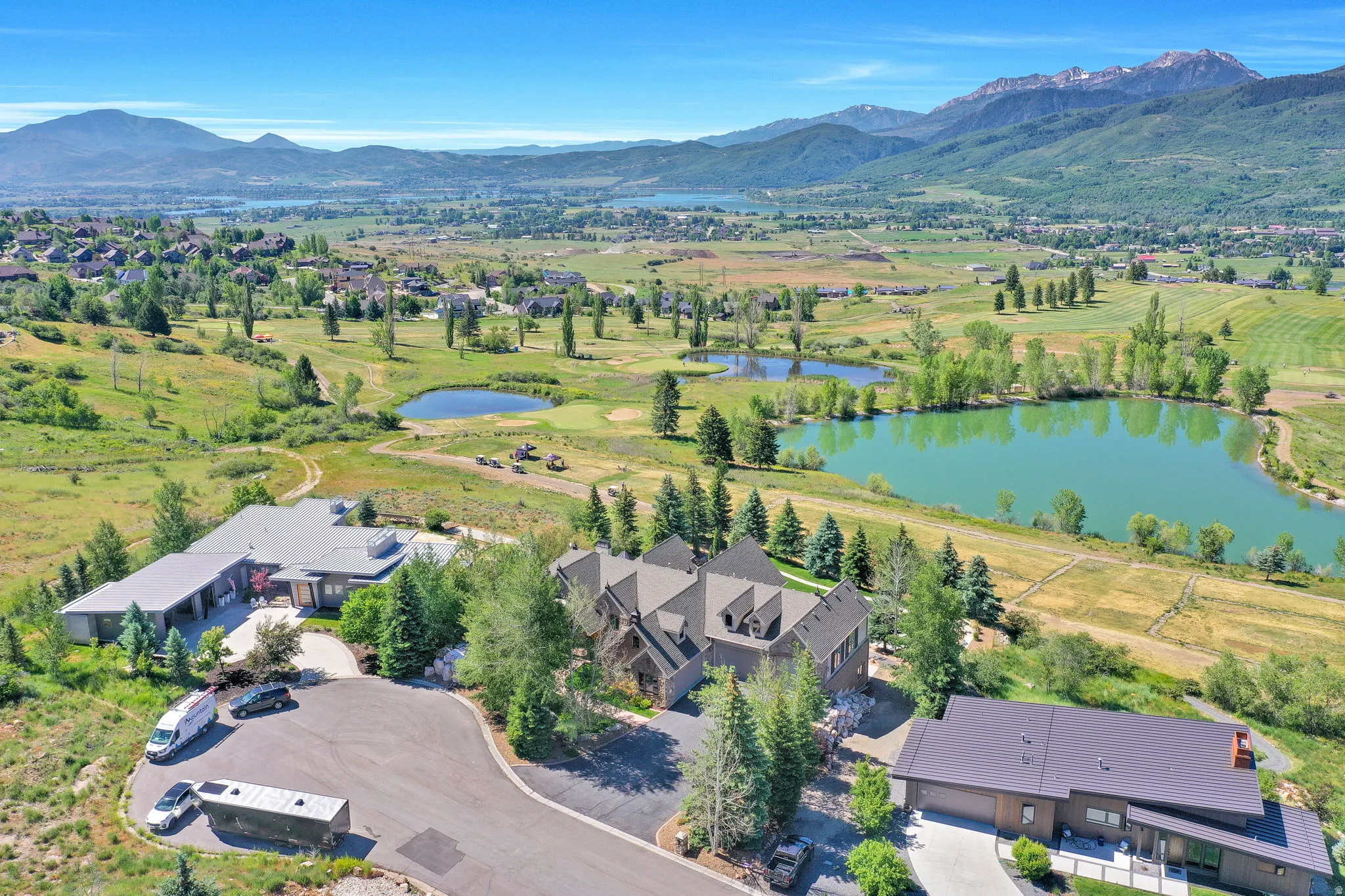 Expansive property featuring multiple architectural styles, a paved drive, mature evergreen landscaping, and surrounding mountainous terrain
