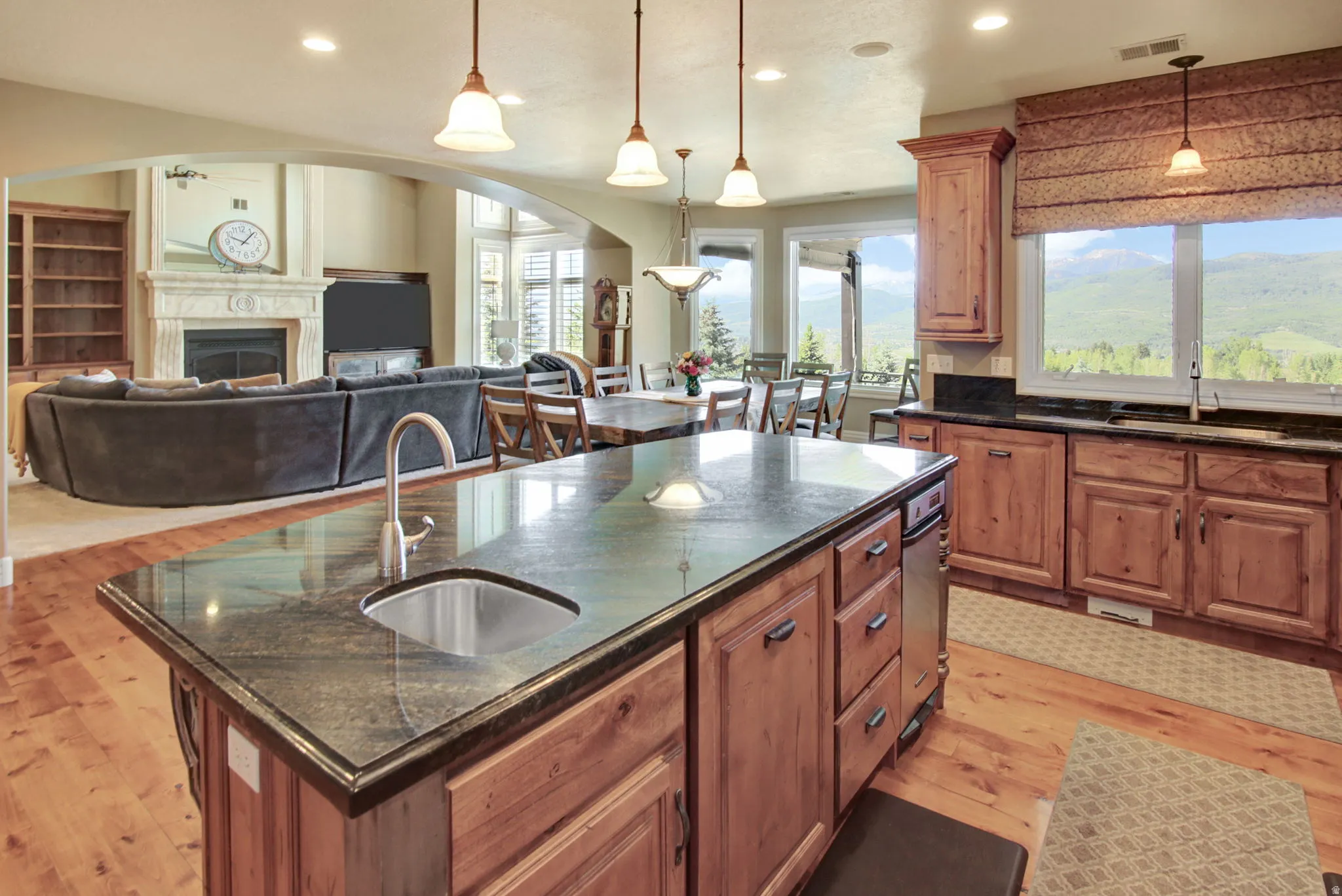 Kitchen island with an undermount sink and dark countertop, wood-finish flooring, wood cabinetry, recessed lighting, and expansive windows