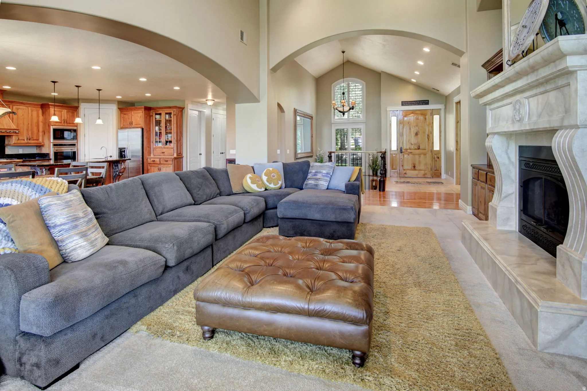 Open-concept living area featuring a stone fireplace with decorative mantel, vaulted ceilings, recessed lighting, and arched doorways