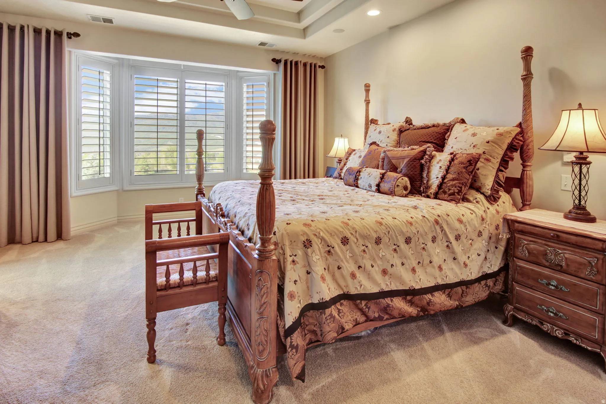 Carpeted bedroom featuring a bay window with plantation shutters, recessed lighting, a ceiling fan, and tray ceiling details
