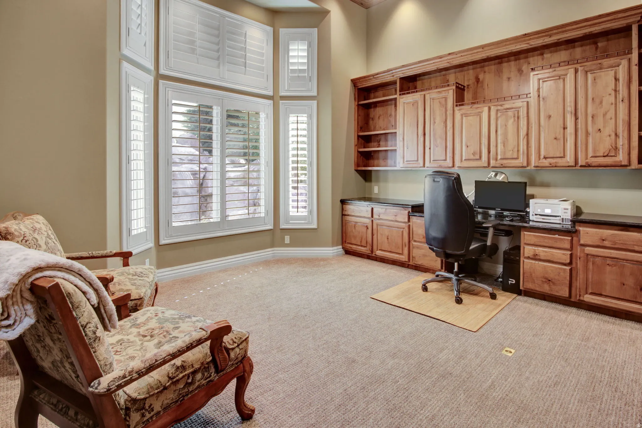 Spacious room featuring a built-in wood cabinetry system, dark countertops, and a bay window with white plantation shutters