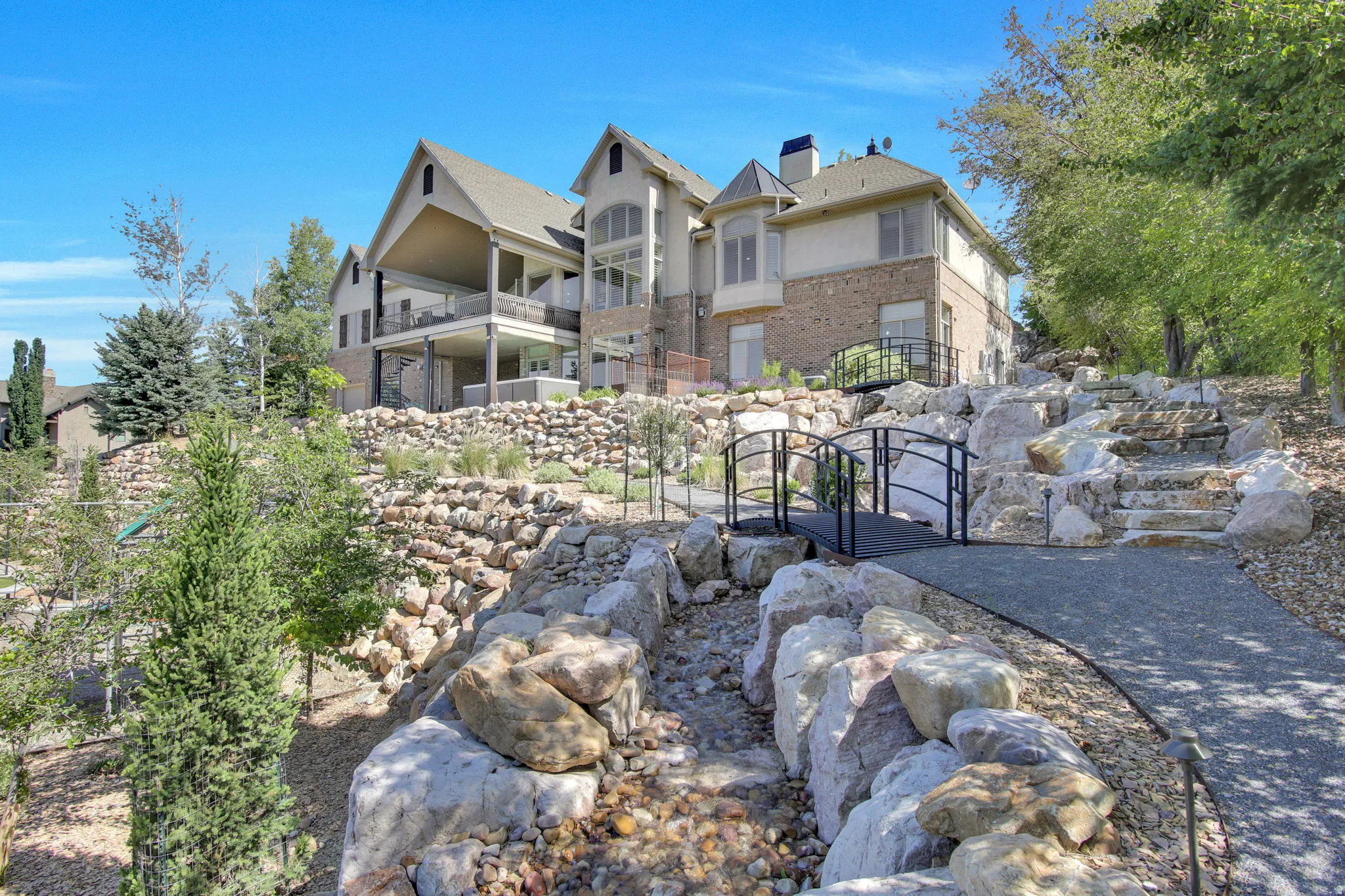 Expansive terraced yard featuring a rock garden, multiple bridges, a winding pathway, and mature trees