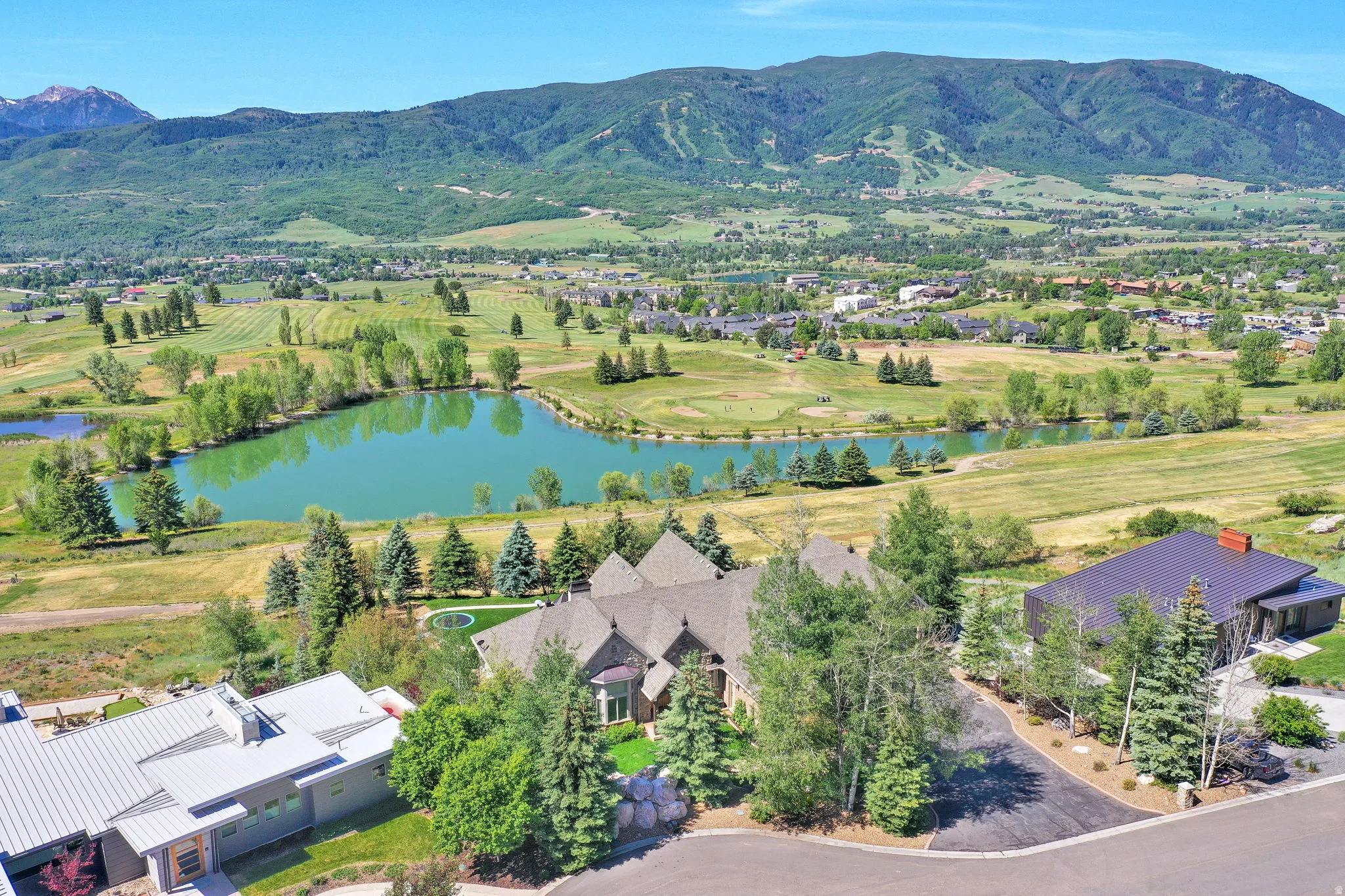 Aerial perspective highlighting the property with a dark shingle roof and multiple gables, situated in a landscaped setting with mature trees