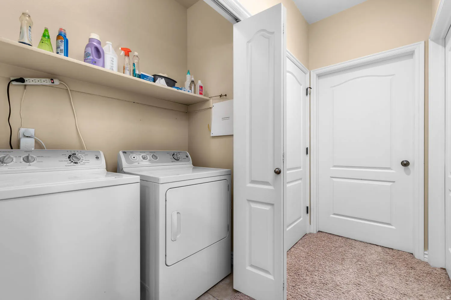 Dedicated laundry area featuring a washer and dryer, an overhead shelf for storage, and multiple white panel doors