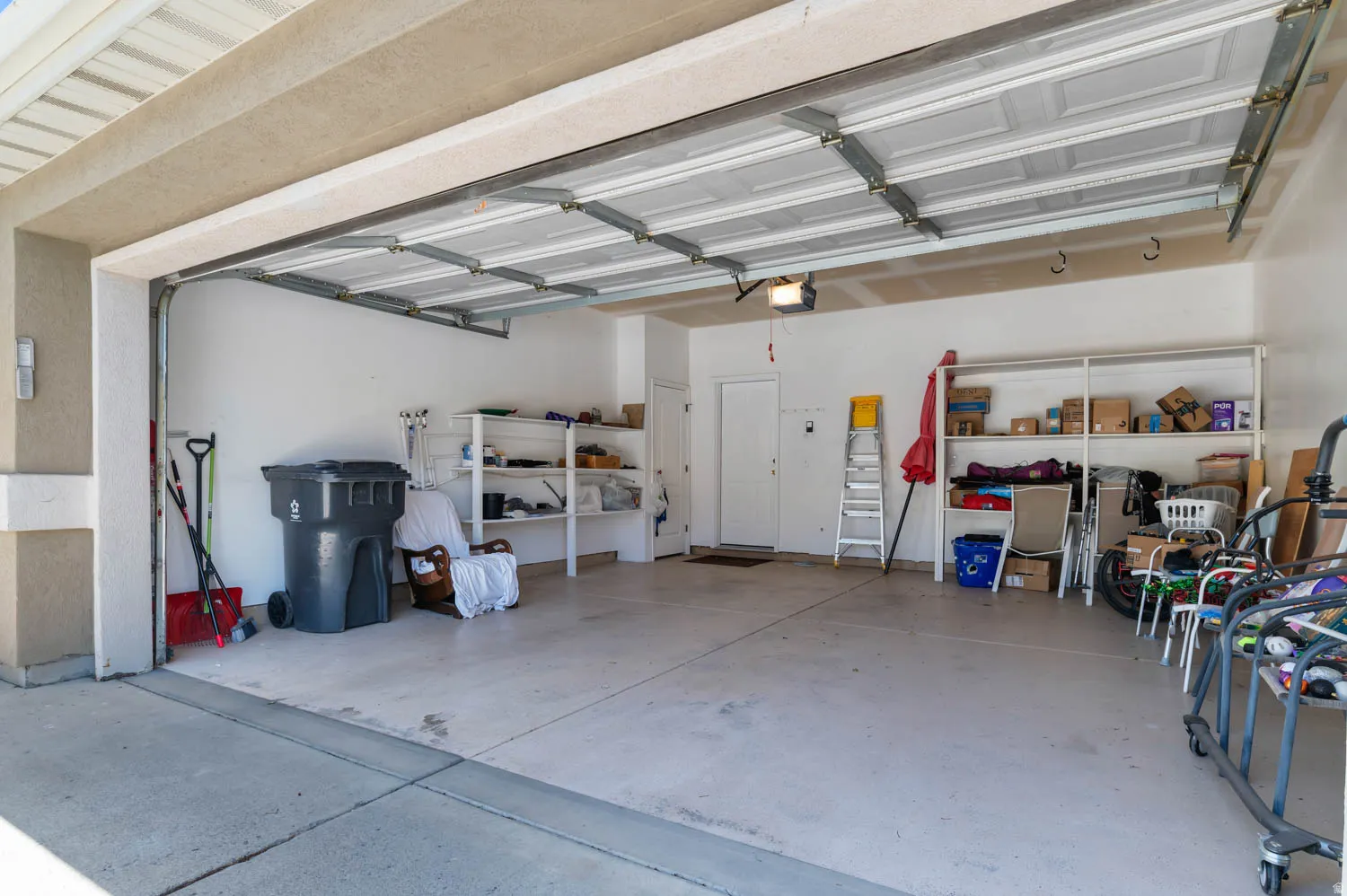 Two-car garage with concrete flooring, automatic garage door opener, interior access door, and built-in shelving
