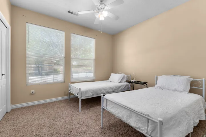 Carpeted room featuring two large windows with blinds, a ceiling fan with integrated lighting, and a white bi-fold closet door
