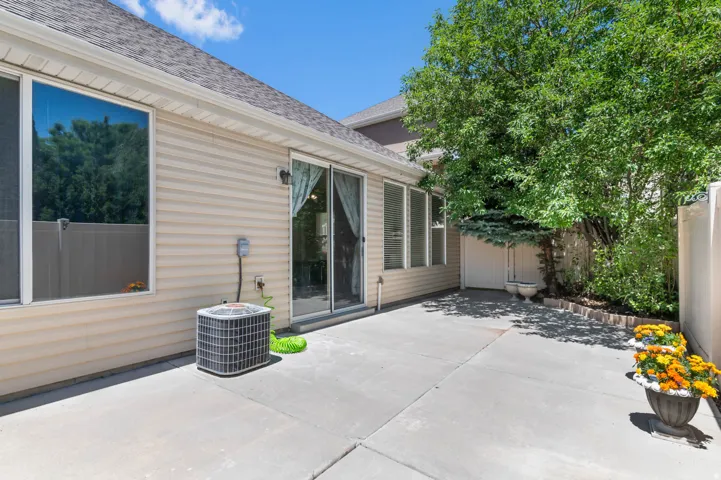 Rear exterior with a concrete patio, vinyl siding, a sliding glass door, and mature trees providing shade