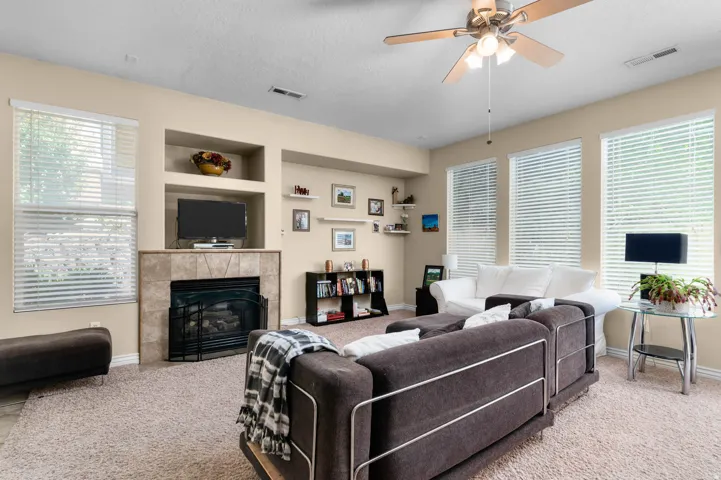 Living area featuring a central fireplace with a tile surround and mantel, built-in shelving, and large windows with blinds