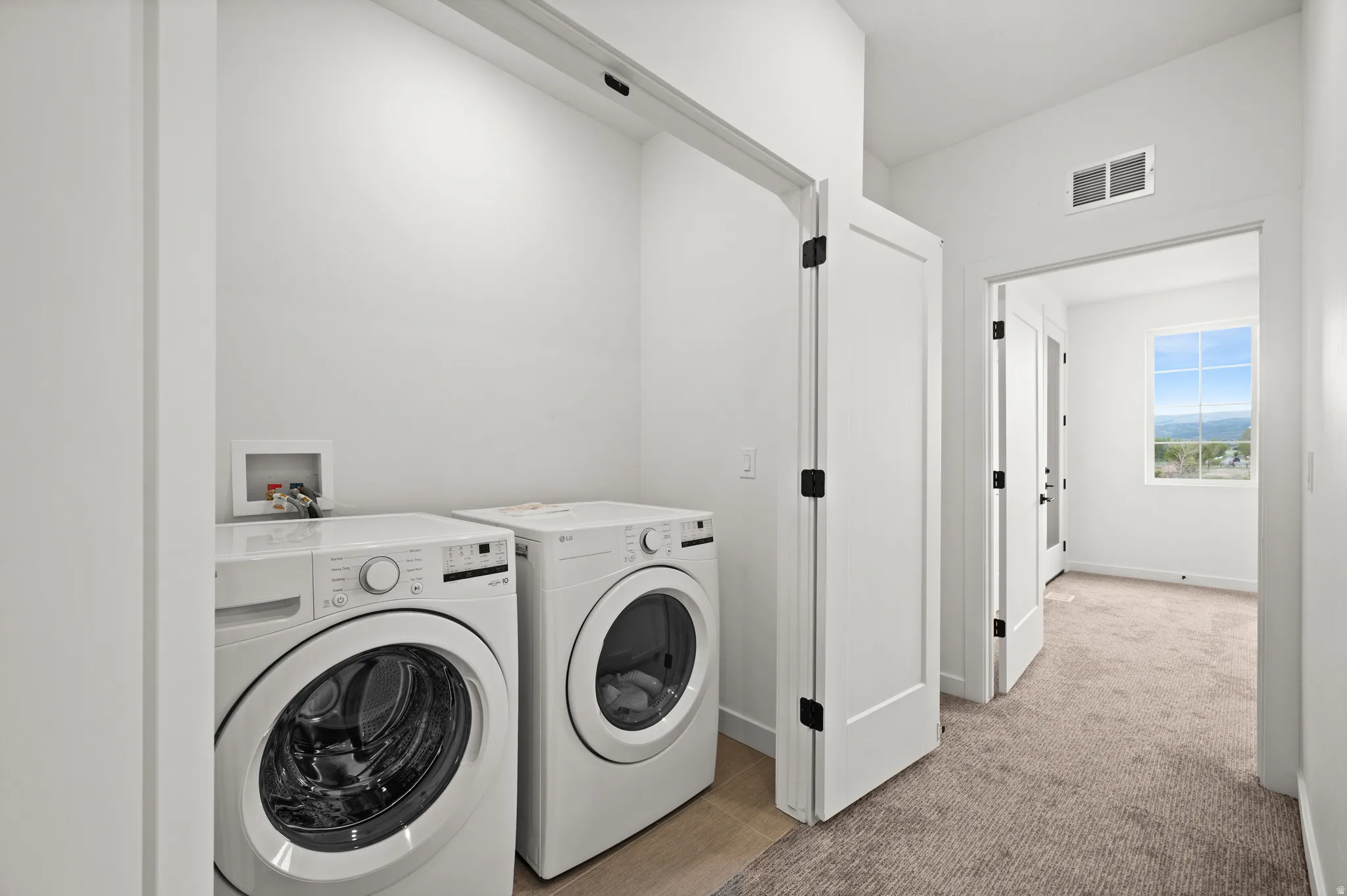 Dedicated laundry area featuring a front-loading washer and dryer, light wood-finish flooring, and bright white walls