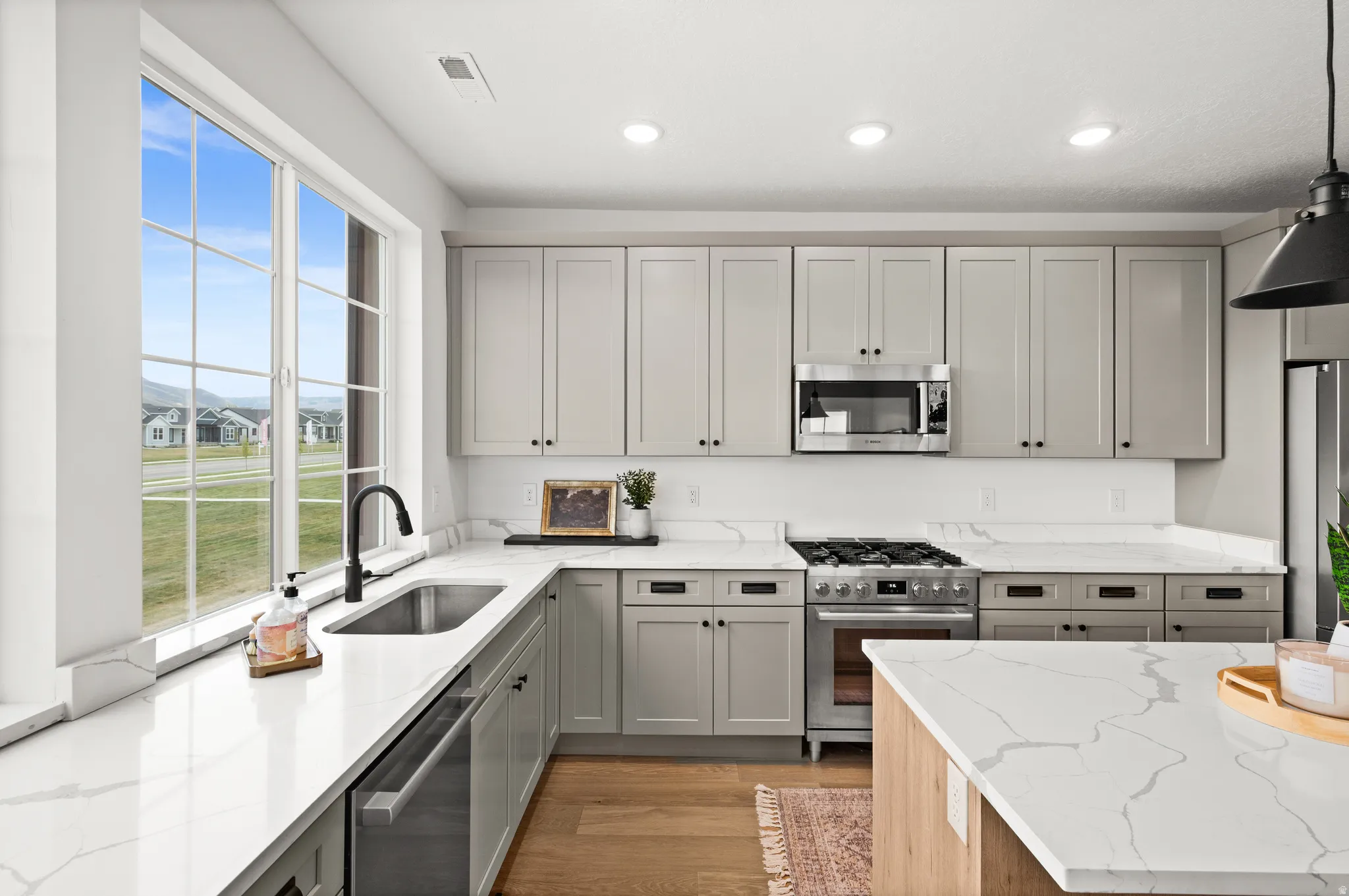 Modern kitchen featuring light gray cabinetry, stainless steel appliances, white countertops with veining, wood-finish flooring, and recessed lighting