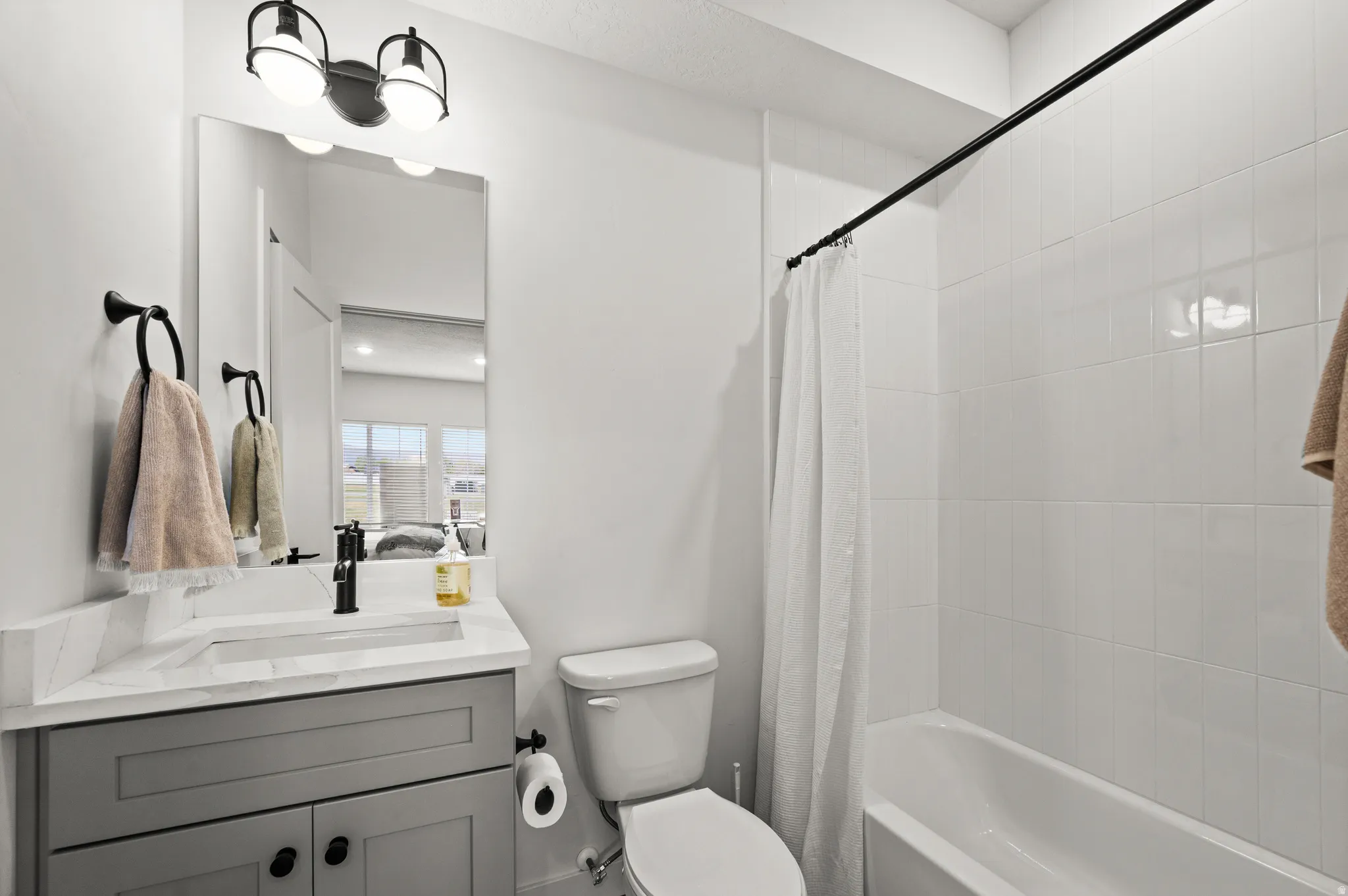 Bathroom featuring a white subway tile shower surround, a white bathtub, and a gray vanity with a white countertop