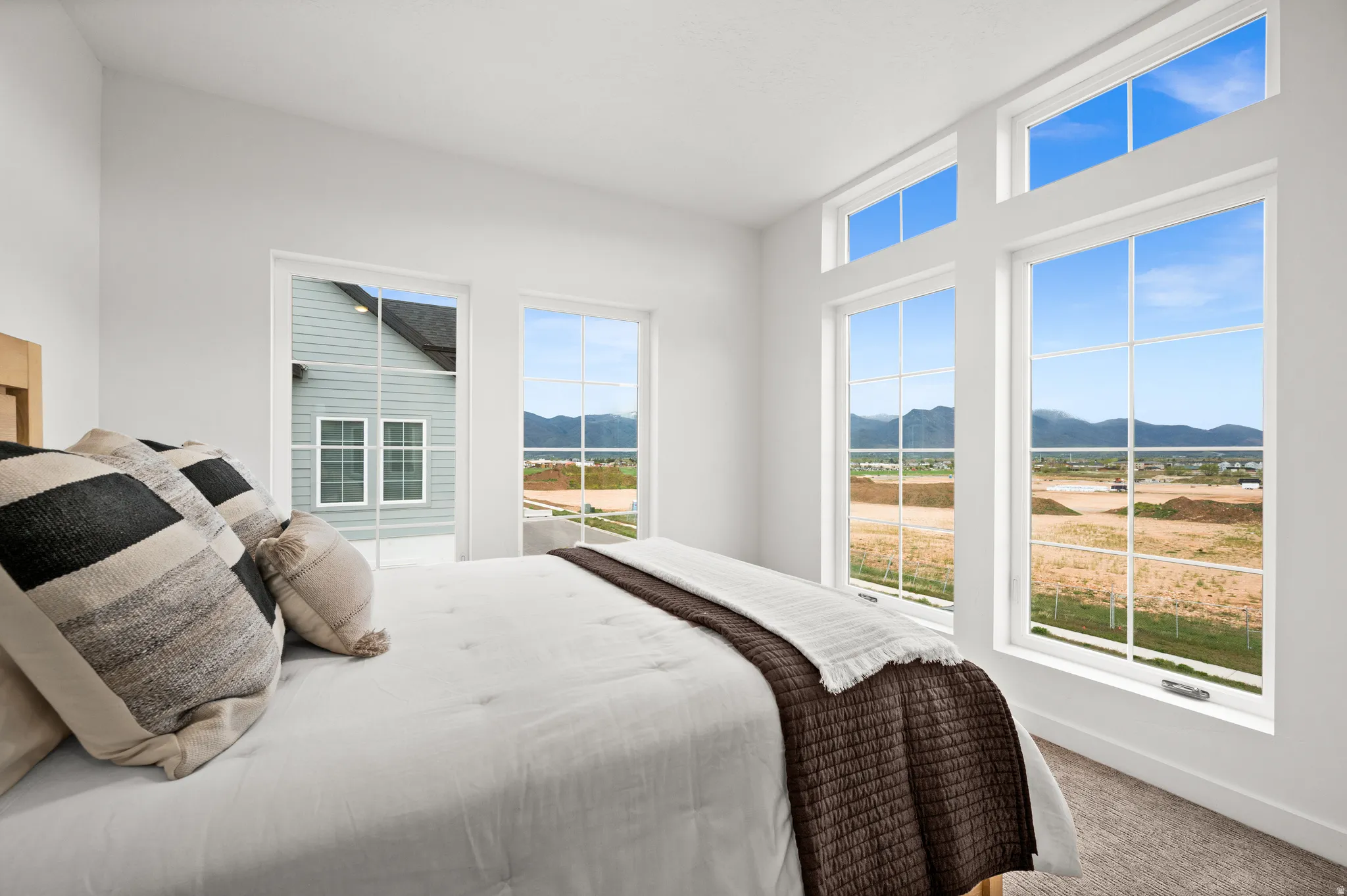 Bright room featuring expansive windows with mountain scenery, a vaulted ceiling, and neutral-toned carpet flooring
