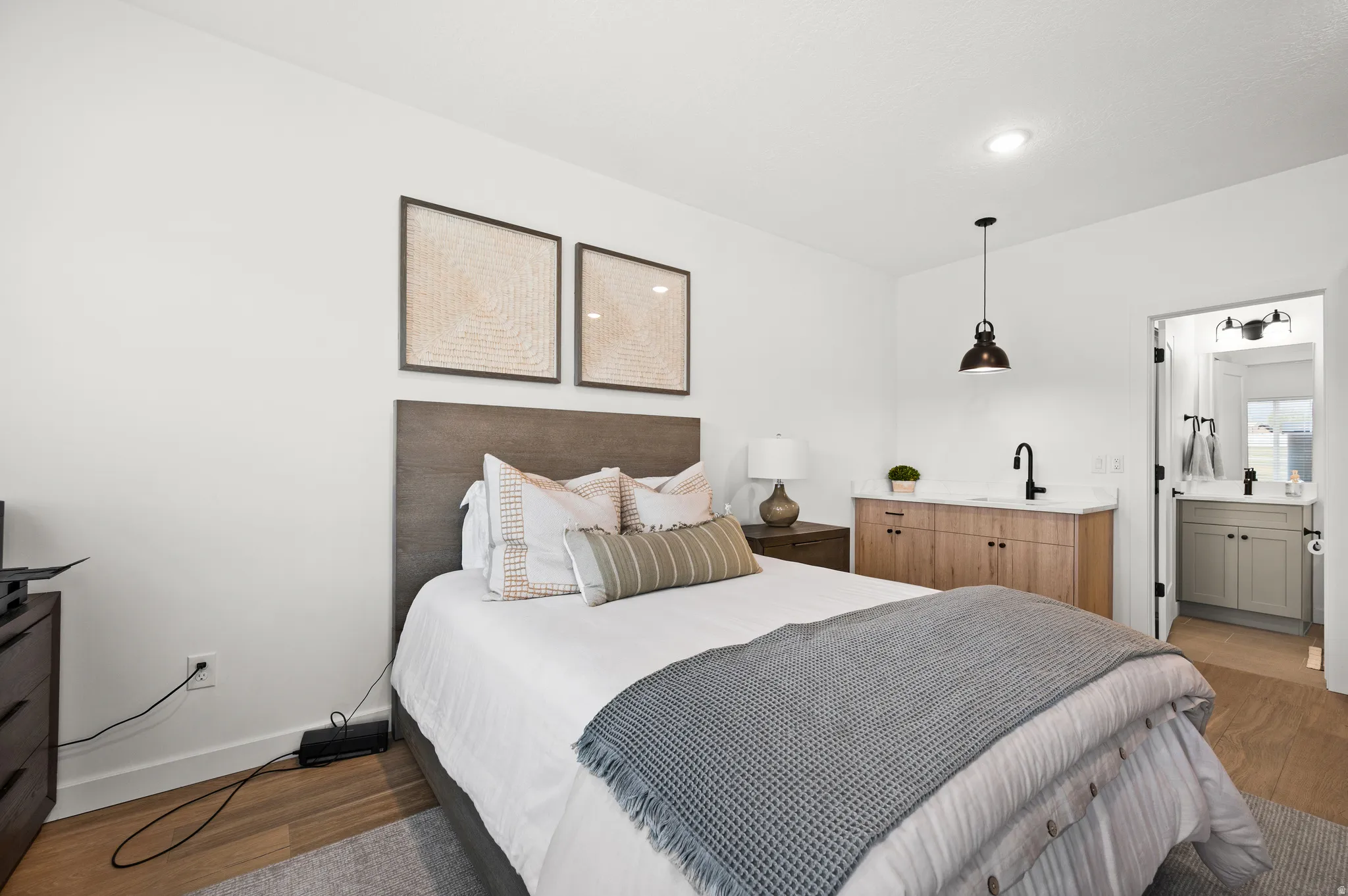Bedroom featuring wood-finish flooring, a built-in wet bar with wood cabinetry, a white countertop, and a black gooseneck faucet