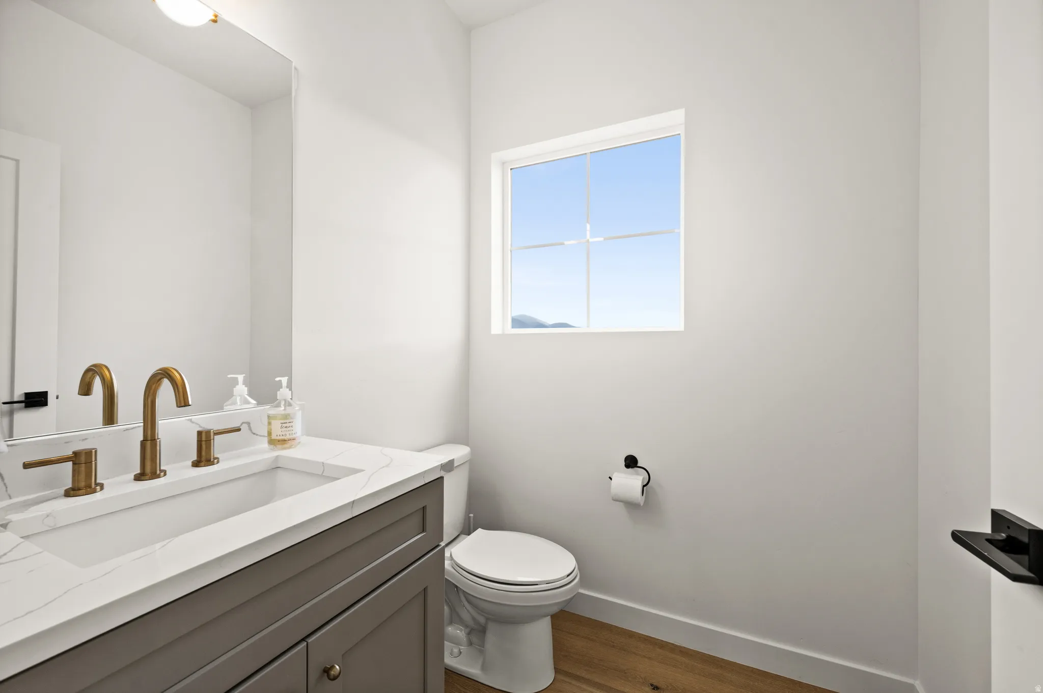Bathroom featuring a grey vanity with a white countertop, an undermount sink, and brass-finish fixtures