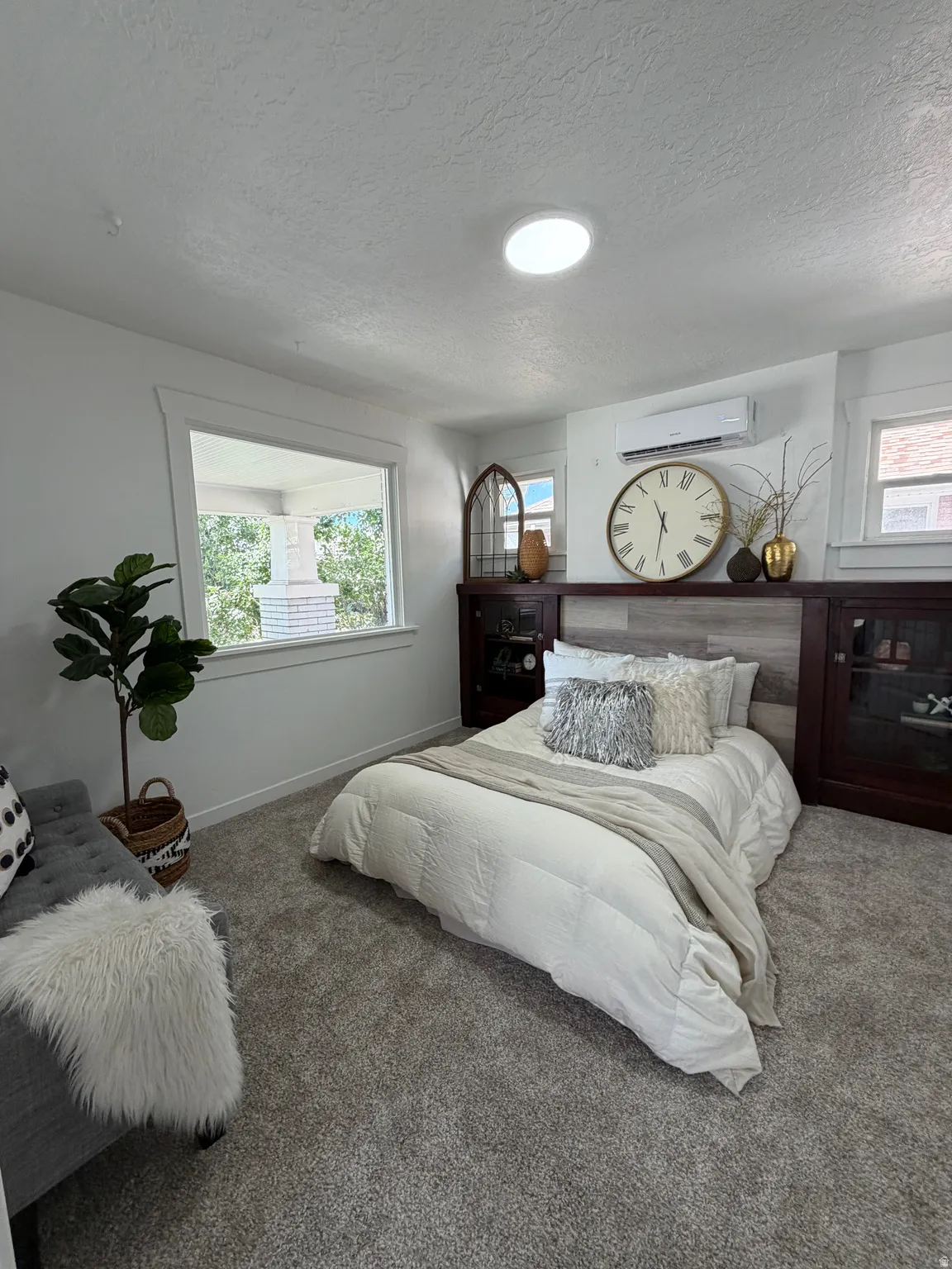 Recessed ceiling lighting, plush gray carpeting, built-in dark wood cabinetry with glass fronts, wood-finish accent wall, and a ductless mini-split system