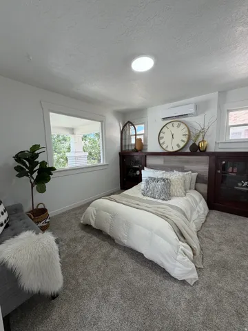 Recessed ceiling lighting, plush gray carpeting, built-in dark wood cabinetry with glass fronts, wood-finish accent wall, and a ductless mini-split system
