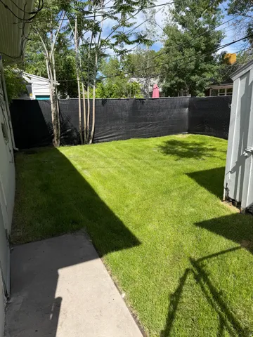 Expansive backyard featuring a green lawn, mature trees, concrete patio, and dark privacy fencing
