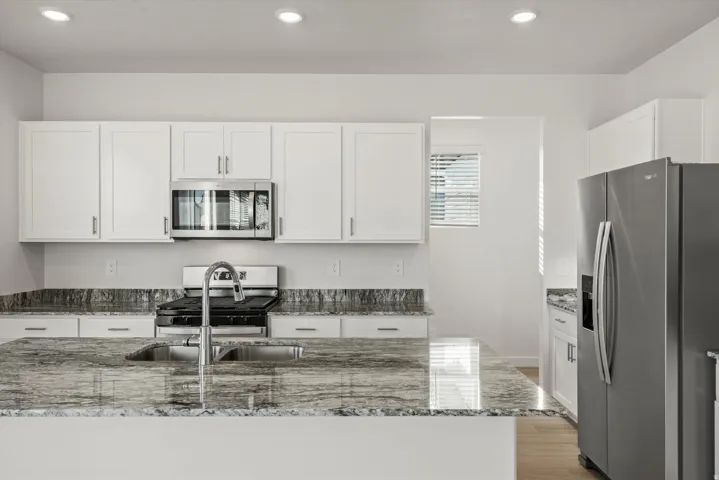 Kitchen featuring an island with an integrated sink, polished chrome faucet, and stone countertop