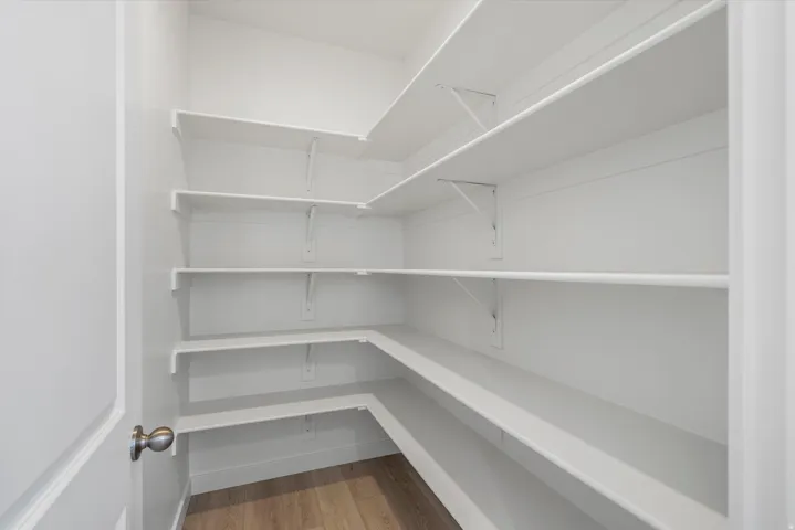 Pantry storage with white shelving, wood-finish flooring, and white trim