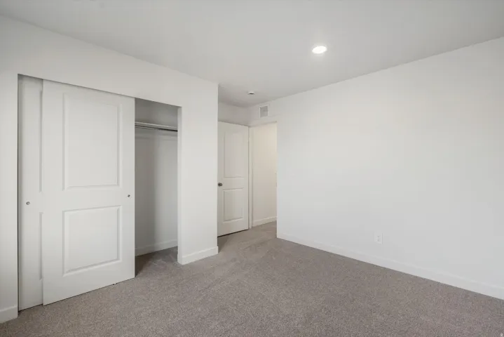 White paneled sliding closet doors, built-in closet shelving and hanging rod, light gray carpeting, recessed ceiling lighting, and white walls