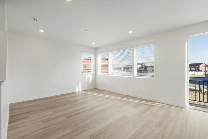 Bright interior space featuring light wood-finish flooring, recessed lighting, multiple windows with blinds, and a sliding glass door with a balcony
