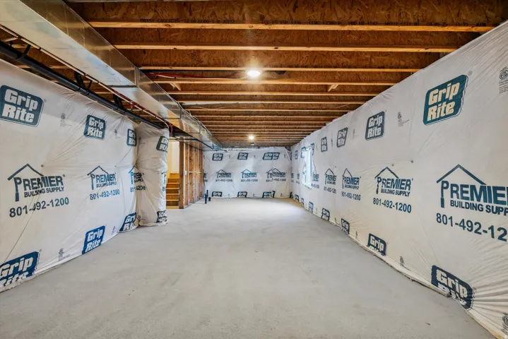 Unfinished basement space with exposed wooden ceiling joists, concrete flooring, and insulated walls