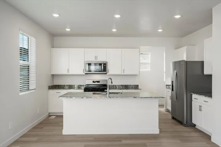Kitchen featuring white cabinetry, a central island with a sink, stainless steel appliances, speckled countertops, and recessed lighting