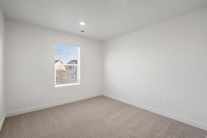 Neutral color palette room featuring light beige carpeting, white walls, and a single window with horizontal blinds