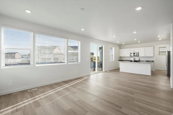Open-concept living space featuring wood-finish flooring, recessed lighting, and a kitchen with white cabinetry, stainless steel appliances, and a central island with a stone countertop