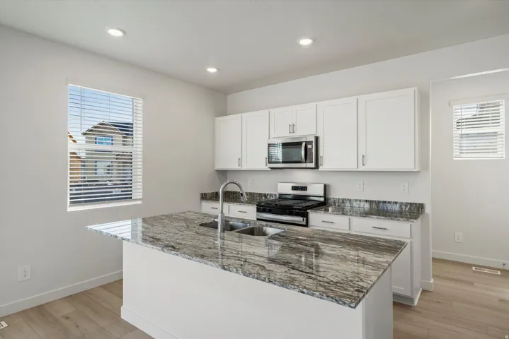 Kitchen featuring a spacious island with an undermount double-basin sink, stainless steel appliances, white cabinetry, and light wood-finish flooring