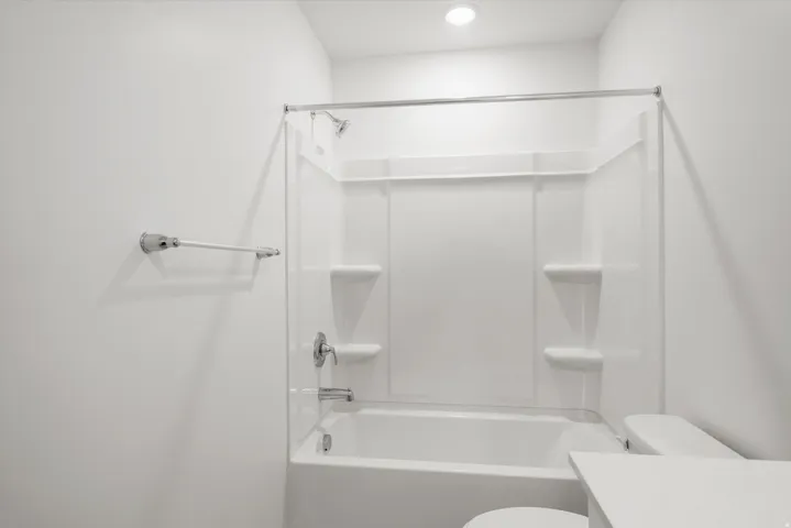 White bathtub and shower combination unit featuring an integrated showerhead, bathtub faucet, and built-in shelving