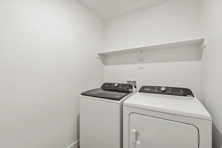 Dedicated laundry area featuring a white washer and dryer, integrated wall shelving, and light-toned walls