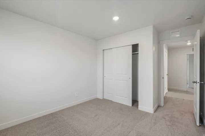 Neutral color palette with recessed lighting, light-toned carpeting, and a closet with sliding panel doors
